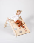 foldable montessori climbing triangle in a sunlit playroom, toddler gripping the sturdy birch rungs with determination