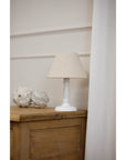 Cyrene table lamp with white wooden base and oatmeal shade, warm beige lighting for cozy home decor by Sostter at brixbailey.com
