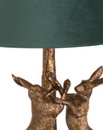 Antique gold marching hare lamp with green velvet shade, handcrafted resin sculpture casting warm ambient glow when lit. by RoomLondon at brixbailey.com