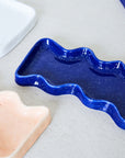 blue speckled ceramic wave tray on a wooden table, sunlight highlighting its playful texture