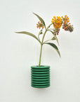 bold green ribble wall vase mounted on a bright white wall with a single fresh flower