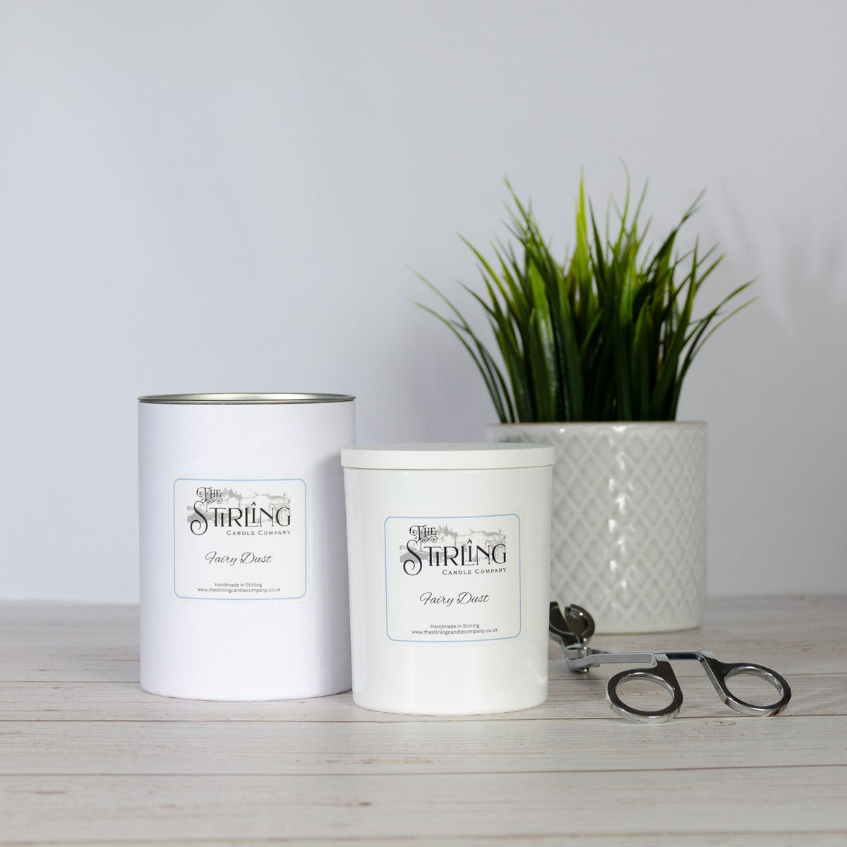 Two white candle tins from The Stirling Candle Company beside a potted plant and a pair of round glasses, on the Brix + Bailey journal.