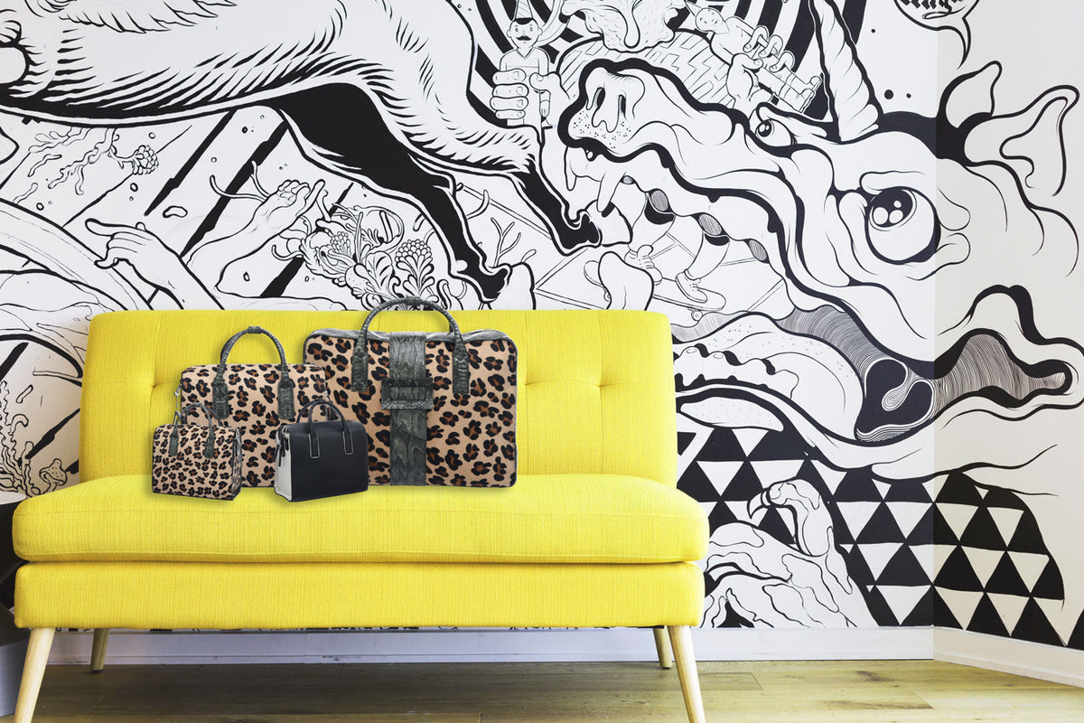 Leopard print and black handbags arranged on a yellow sofa against a black and white mural