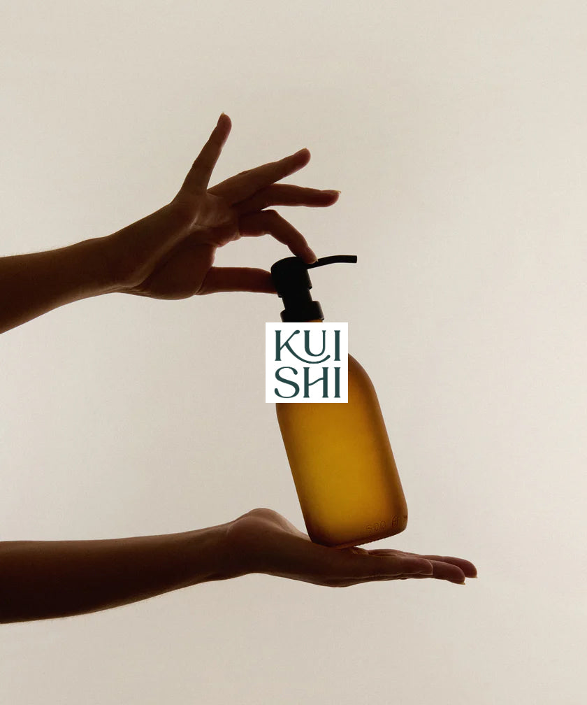 Hands pressing a Kuishi refillable amber glass dispenser.