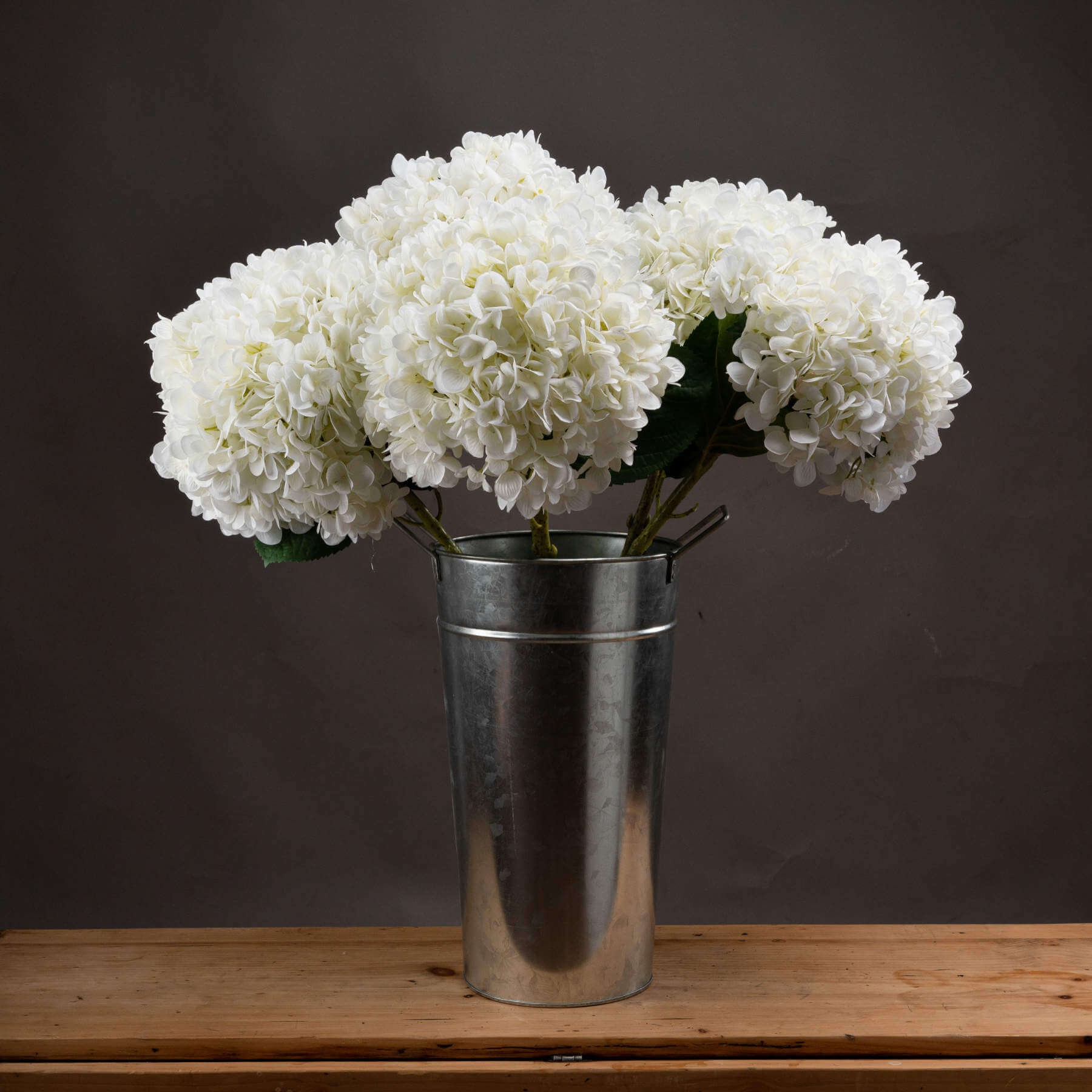 white hydrangea flowers from Brix + Bailey marketplacearranged in a silver metal vase on wooden table