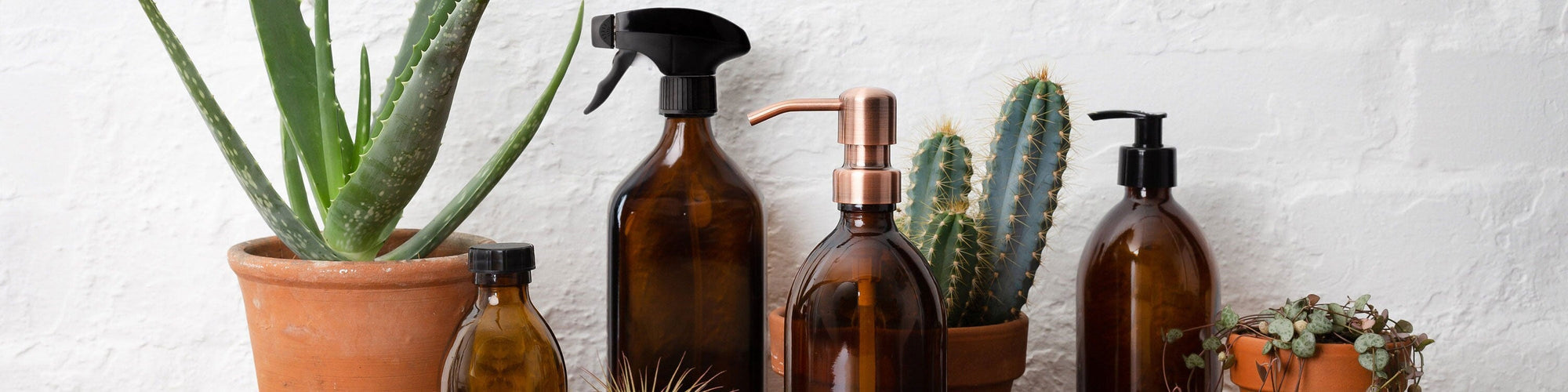 Amber glass refillable spray bottles and wooden bristle brushes arranged on a kitchen counter