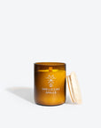 softly lit friga candle in amber glass casting a warm, cozy glow on a rustic wooden table
