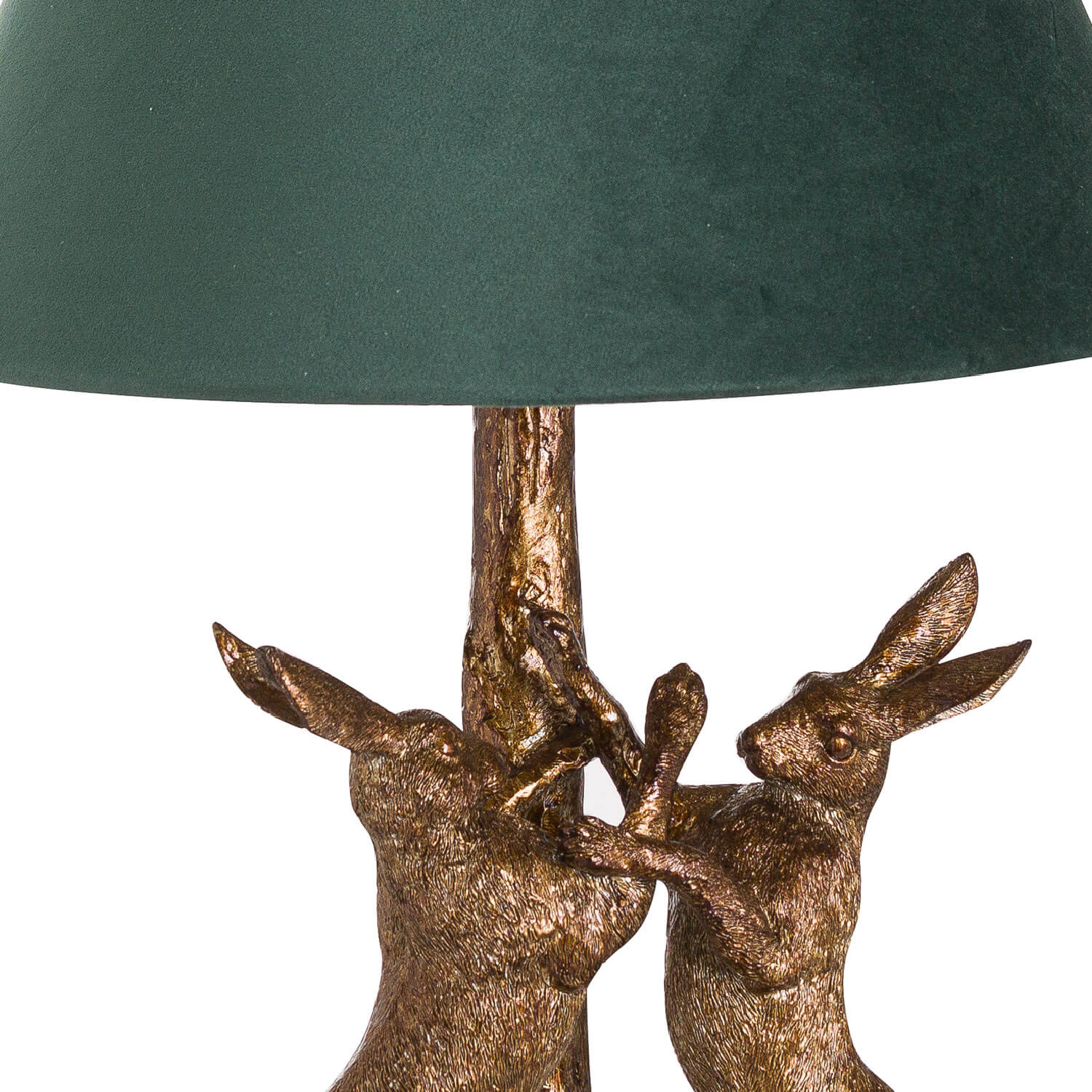 Antique gold marching hare lamp with green velvet shade, handcrafted resin sculpture casting warm ambient glow when lit. by RoomLondon at brixbailey.com