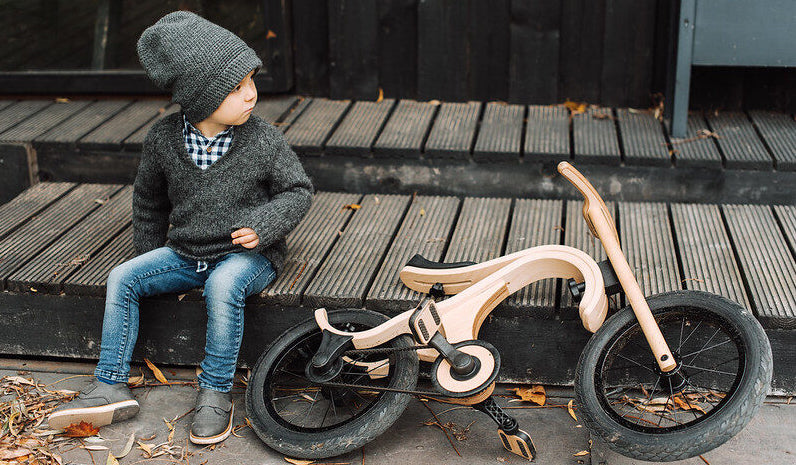 Child sitting on a wooden step beside a wooden balance bike