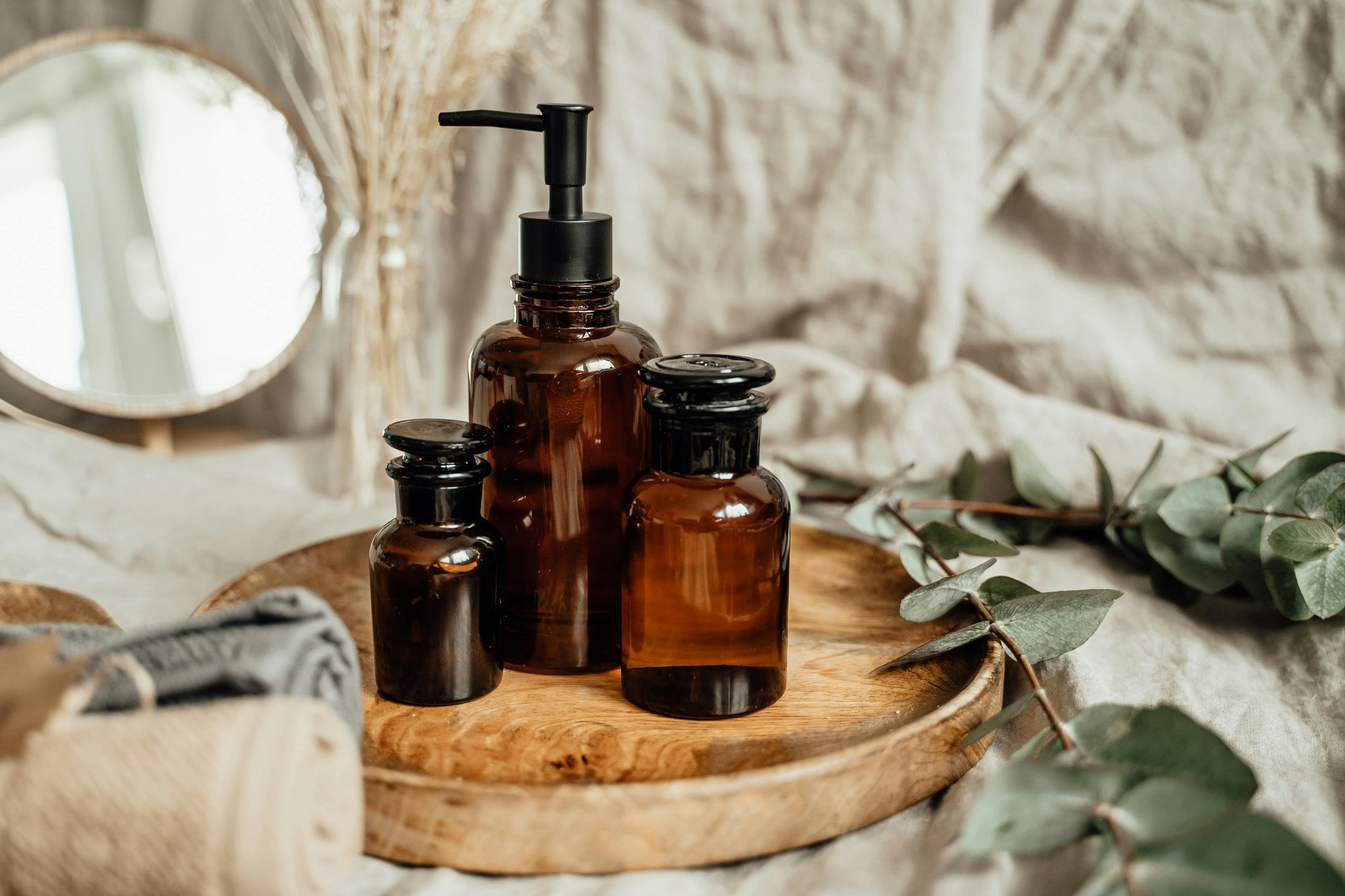 Set of Kuishi brown glass bottles with black caps on a wooden tray, surrounded by greenery and fabric.