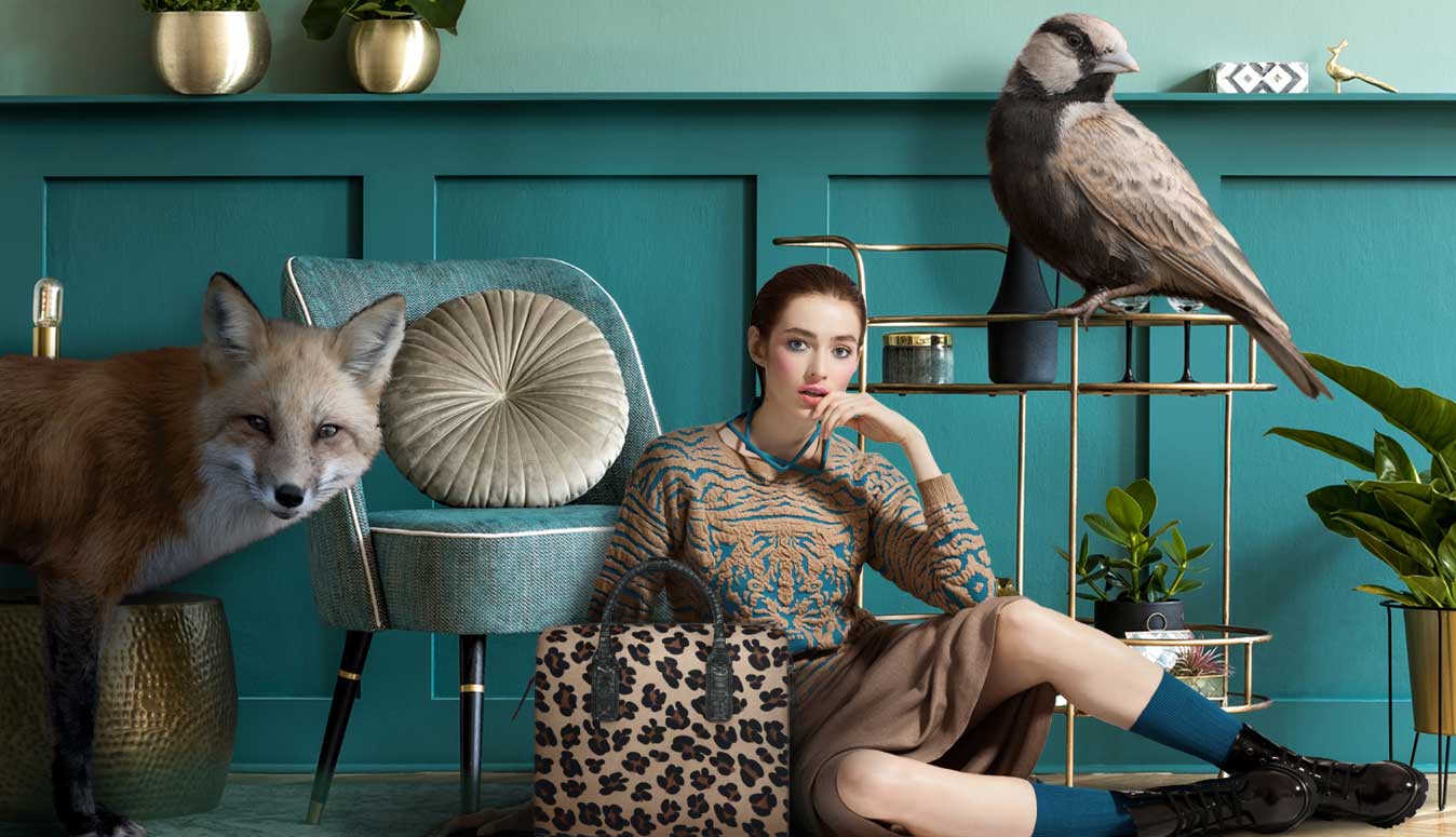 Styled woman sitting with leopard-print bag, fox and bird in a teal interior — Brix + Bailey fashion and home curation
