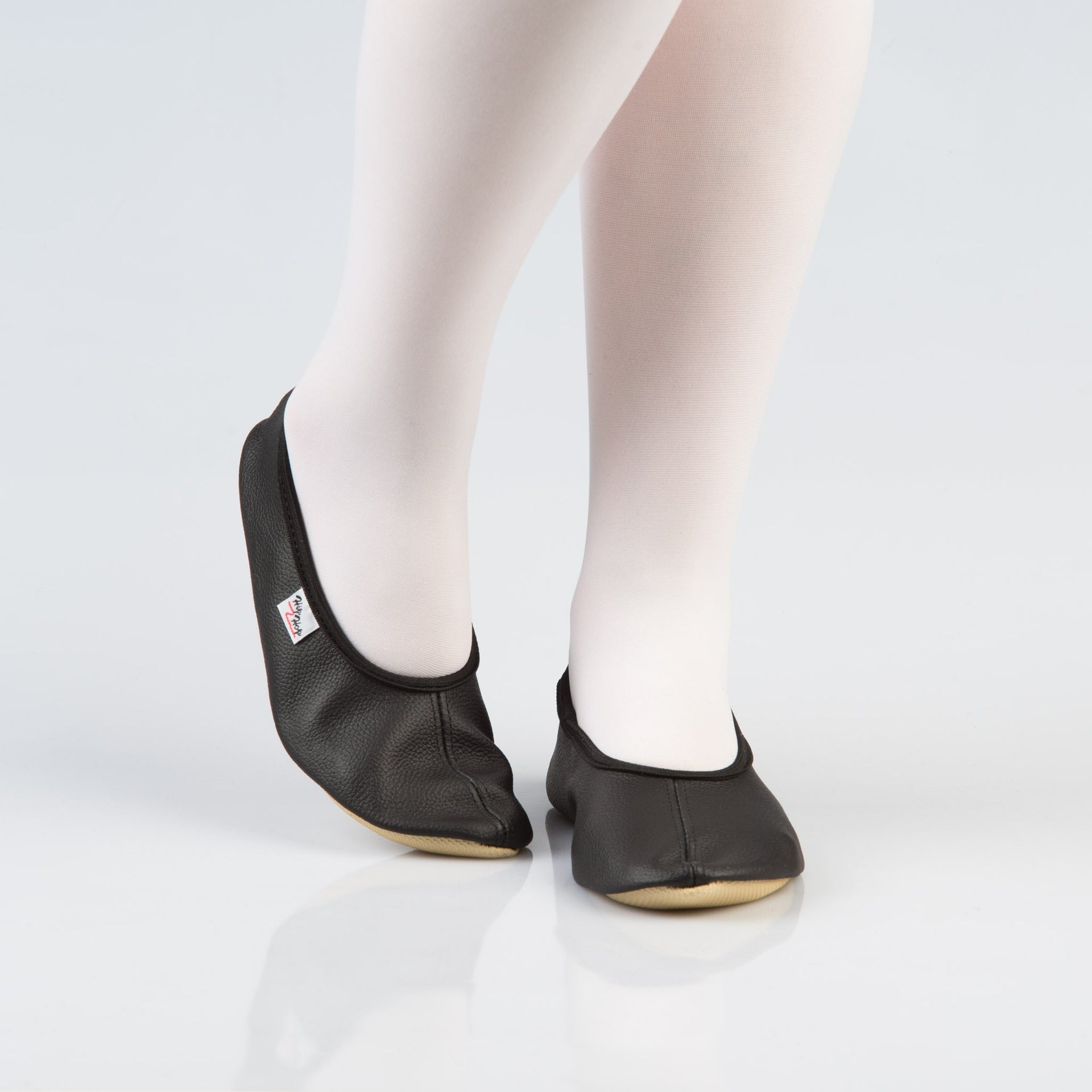 soft black leather gymnastics slippers with a secure rubber edge, resting on a cozy surface