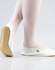 white leather gymnastics slippers with bold rubber sole on a dark studio floor