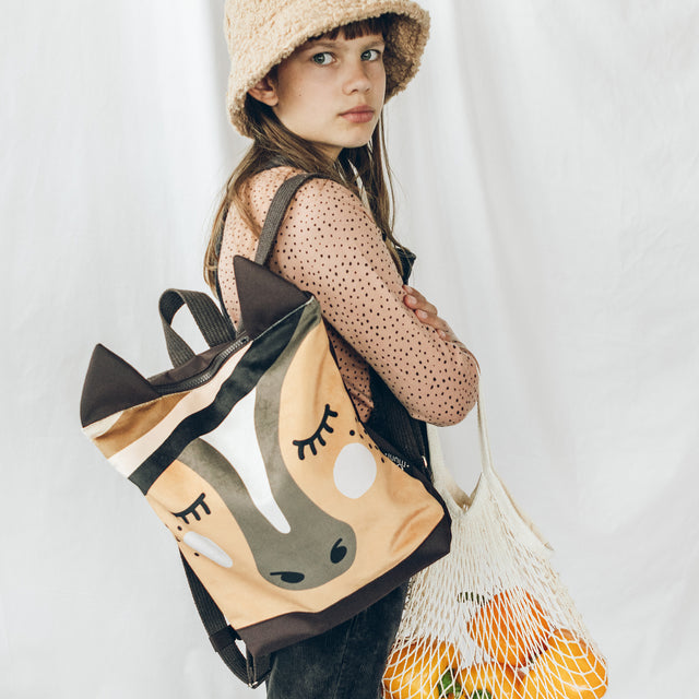 Child wearing beige bucket hat modeling Muni horse-shaped backpack with polka dot shirt and yellow mesh bag from Brix + Bailey marketplace