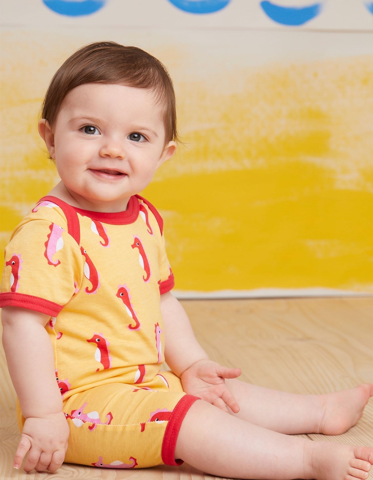 Luxury baby romper with short legs, stylish seahorse design, red trim, snap buttons, organic cotton, sustainable fashion by Toby Tiger at brixbailey.com